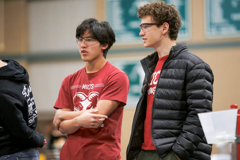 Ryan Jan talking with a teammate at an FTC robotics competition, both wearing safety glasses.